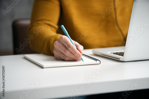 Close up shot of young business man hands with pen writing notes on a paper. Male executive sitting at table at office