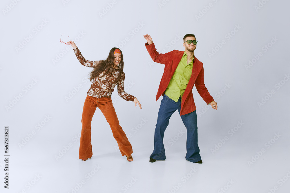 Naklejka premium Having fun. Stylish young man and woman in colorful retro outfits dancing disco dance isolated over grey studio background. 70s fashion, hobby, creativity, hippie lifestyle, American culture
