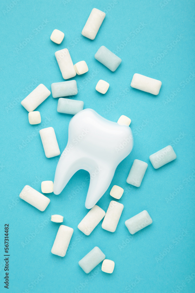 Obraz premium White healthy tooth model and heap of chewing gums on blue background. Concept of oral dental hygiene Vertical photo