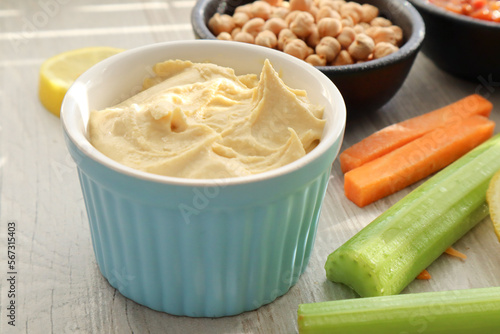 Bowl of hummus with celery sticks and carrot sticks in the foreground 