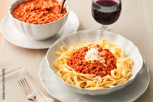 Plate of fresh tagliatelle pasta with bolognese sauce and wine glass on a linen tablecloth. Low angle view. Studio shot.