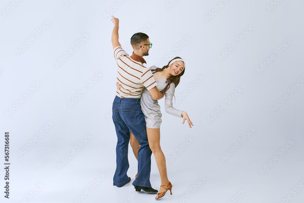 Romantic look. Young beautiful girl in silver dress and stylish man dancing disco dance isolated over grey studio background. 70s fashion, hobby, creativity, hippie lifestyle, American culture Romantic look. Young beautiful girl in silver dress and stylish man dancing disco dance isolated over grey studio background. 70s fashion, hobby, creativity, hippie lifestyle, American culture