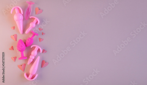 Pink silicone sex toys and paper heart on a pink background. the concept of valentine's day, love. Erotic toy for fun. Diffrent anal butt plugs. Banner with space for text