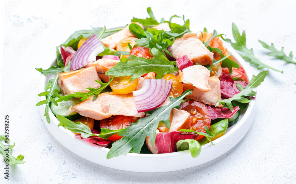 Grilled salmon fish salad with tomato, cucumber, arugula, radicchio, red onion and lettuce with lemon and sesame seeds. Healthy eating delicious lunch. White table background, top view