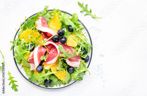 Gourmet salad with smoked duck, oranges, blueberries, arugula and lettuce, white table background, top view