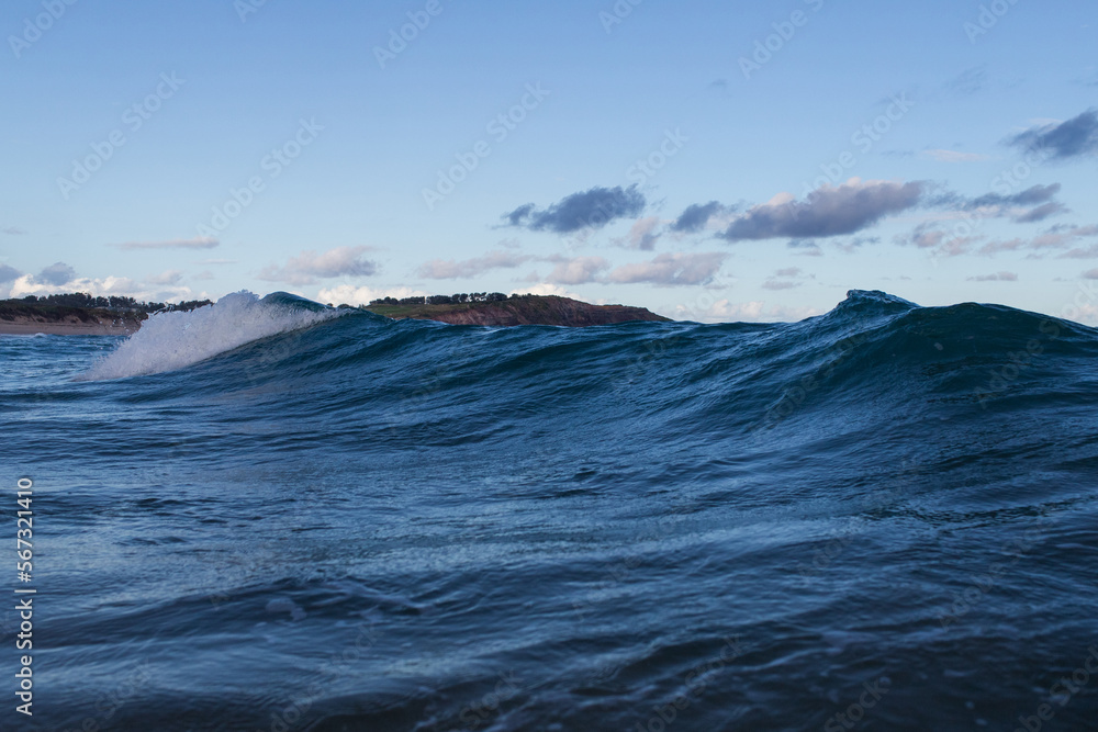 Long reef headland behind blue wave, Sydney, Australia.