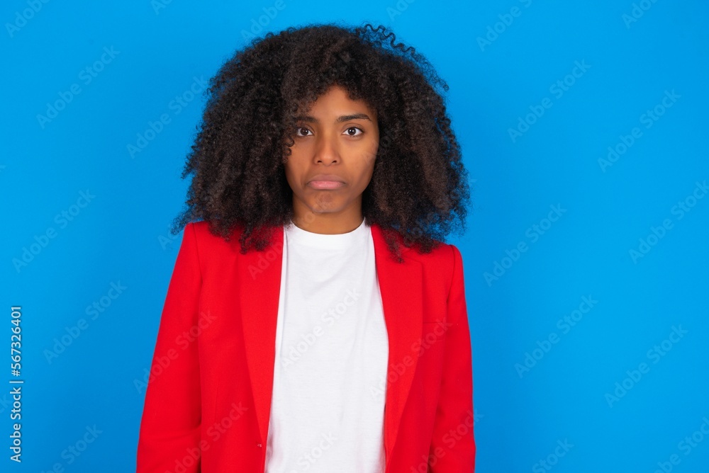 young businesswoman with afro hairstyle wearing red over blue background crying desperate and depressed with tears on his eyes suffering pain and depression. Sad facial expression and emotion concept. young businesswoman with afro hairstyle wearing red over blue background crying desperate and depressed with tears on his eyes suffering pain and depression. Sad facial expression and emotion concept.