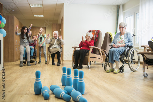 Girls playing bowling with senior women in rest home photo