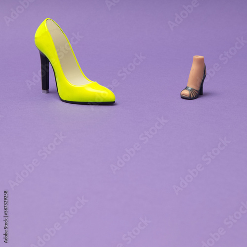 A yellow female heel on a purple background and a slightly smaller heel with a female foot, with copy space. Minimal women scene.
