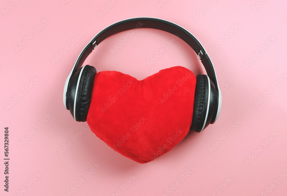flat lay of red heart pillow coverd with headphones on pink background. Love songs or podcast concept. flat lay of red heart pillow coverd with headphones on pink background. Love songs or podcast concept.