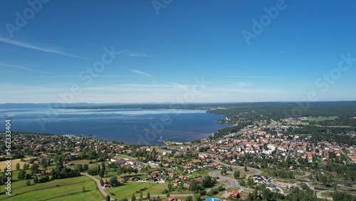 Panoramic view of a picturesque town on the mountain, on a beautiful blue lake with a pier. Blue sky with mountains and vast forests in the background. High angle view of a city with red houses