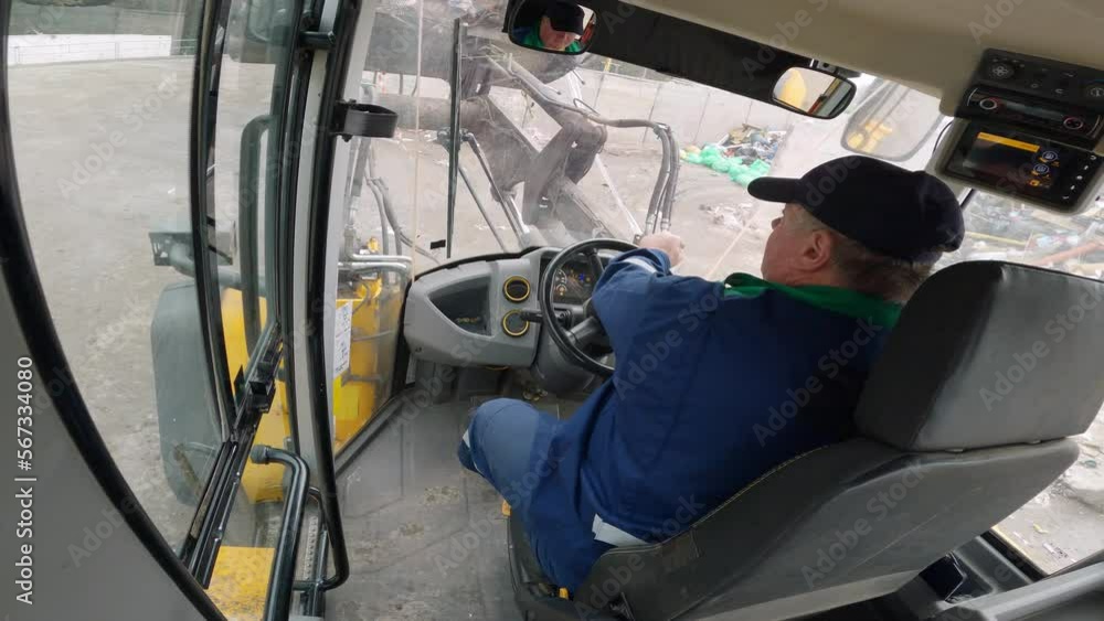 Inside cab view of a man driving heavy machine vehicle, a front loader grabbing garbage and loading a truck, fast motion. Waste management concept. Inside cab view of a man driving heavy machine vehicle, a front loader grabbing garbage and loading a truck, fast motion. Waste management concept.