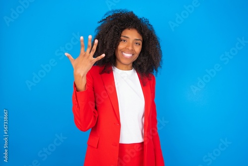 young businesswoman with afro hairstyle wearing red over blue background smiling and looking friendly, showing number five or fifth with hand forward, counting down