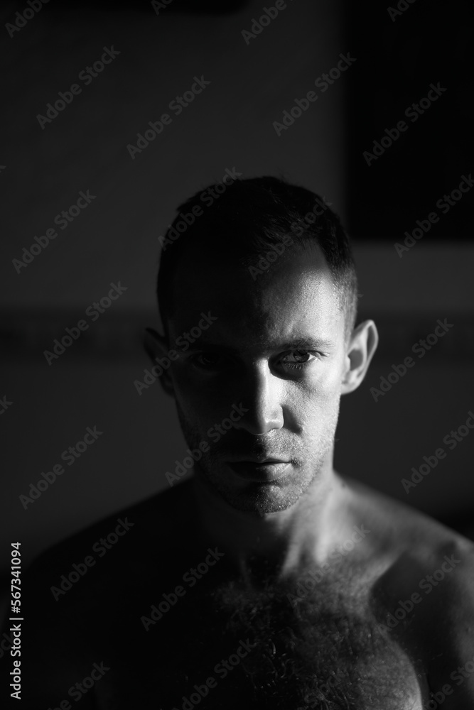 Portrait of handsome man in hard side light facing camera. Half of attractive male face lit by the sun rays on sunrise. Portrait of handsome man in hard side light facing camera. Half of attractive male face lit by the sun rays on sunrise.