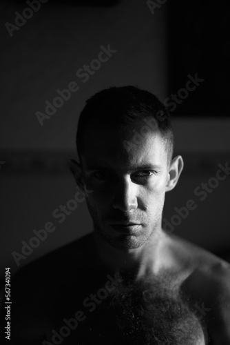 Portrait of handsome man in hard side light facing camera. Half of attractive male face lit by the sun rays on sunrise.