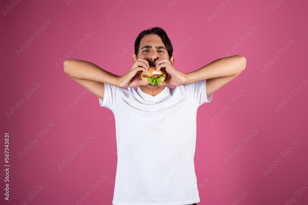 Portrait of a hungry guy in a white shirt with a piece of pizza. Pink background. Fast food. Portrait of a hungry guy in a white shirt with a piece of pizza. Pink background. Fast food.