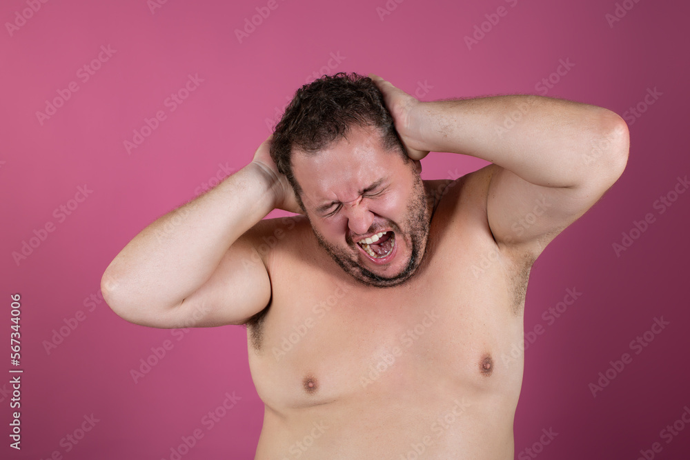 Fototapeta premium Migraine in a fat man on a pink background. Suffering, pain.