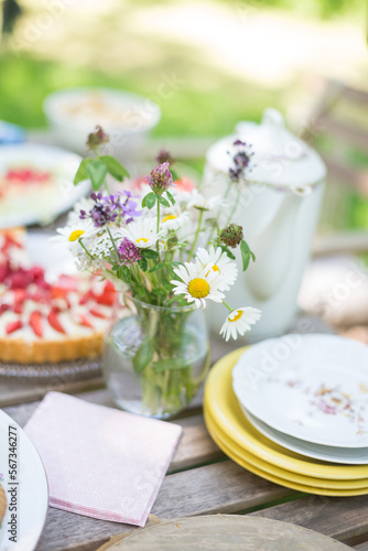 Tisch im Grünen gedeckt mit Erdbeerkuchen und Tellern, einer alten Kaffeekanne und einem Strauß Wiesenblumen