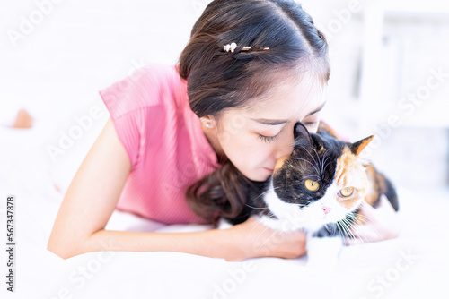 Young beautiful cat lover working woman with cute cat lying in bed at home and having fun on bed