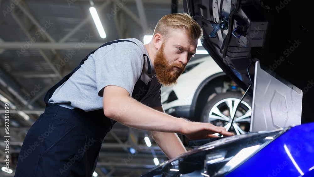 An electrician man during troubleshooting in a car with the help of professional equipment at a service station An electrician man during troubleshooting in a car with the help of professional equipment at a service station