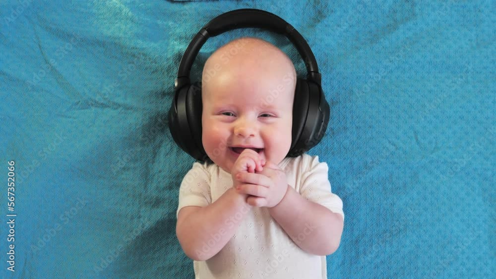 Little boy 4 months old lying on the bed wearing black wireless headphones listening to music and looking at the camera. Little boy 4 months old lying on the bed wearing black wireless headphones listening to music and looking at the camera.