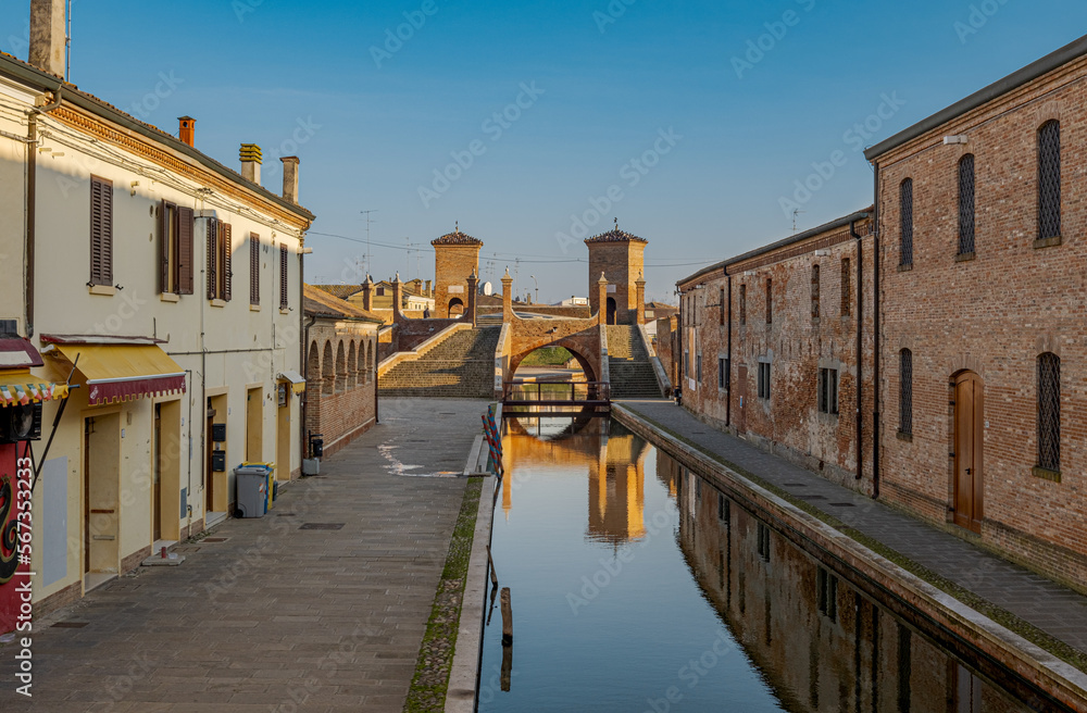 Perspective view of a Comacchio canal with the famous three-ways bridge in the background. Comacchio, province of Ferrara, Emilia Romagna, Italy.