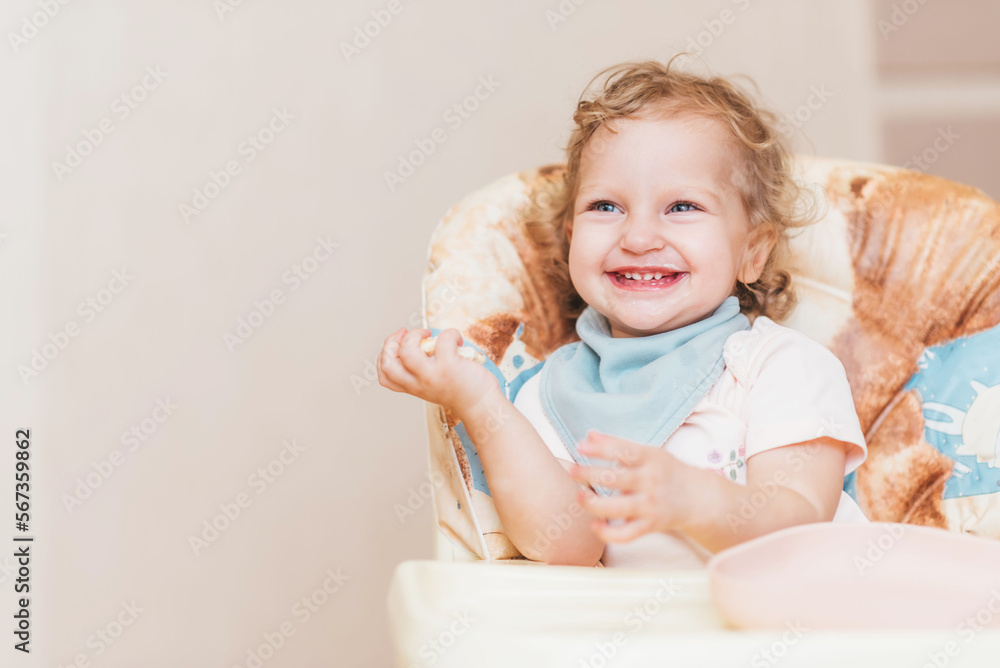 Fototapeta premium Happy little baby eats at home sitting on a chair