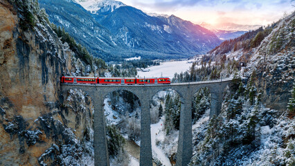 Aerial view of Train passing through famous mountain in Filisur, Switzerland. Landwasser Viaduct world heritage with train express in Swiss Alps snow winter scenery.