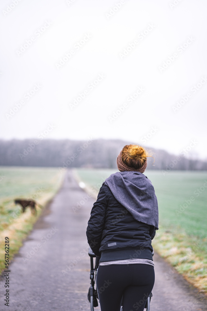 Fototapeta premium Frau mit Kinderwagen und Hund auf einer gerade geteerten Straße unterwegs