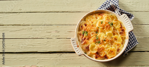 Tableau sur toile Tasty gratin potatoes in ceramic dishware on wooden table