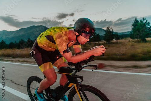 Night drive. Full length portrait of an active triathlete in sportswear and with a protective helmet riding a bicycle in night time.. Selective focus 