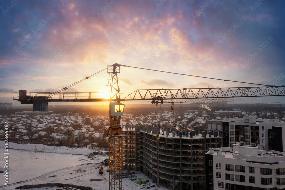 Fototapeta premium Industrial cranes at construction site with dramatic sunset sky background.