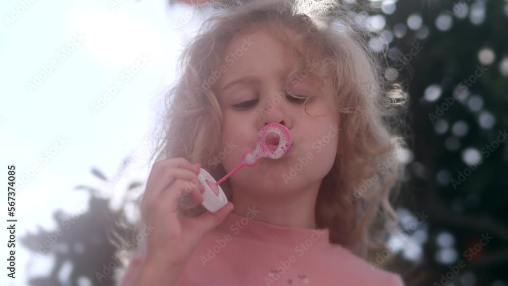 Focused little blonde girl in pink blows soap bubbles Focused little blonde girl in pink blows soap bubbles