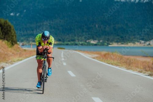 Fototapeta Naklejka Na Ścianę i Meble -  Close up photo of an active triathlete in sportswear and with a protective helmet riding a bicycle. Selective focus