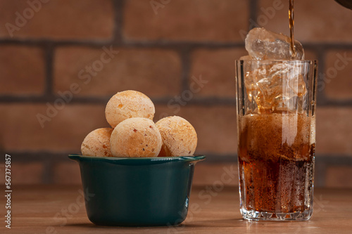 Cheese breads in a green ramekin with a glass of cola soft drink on wooden table and bricks wall background. photo