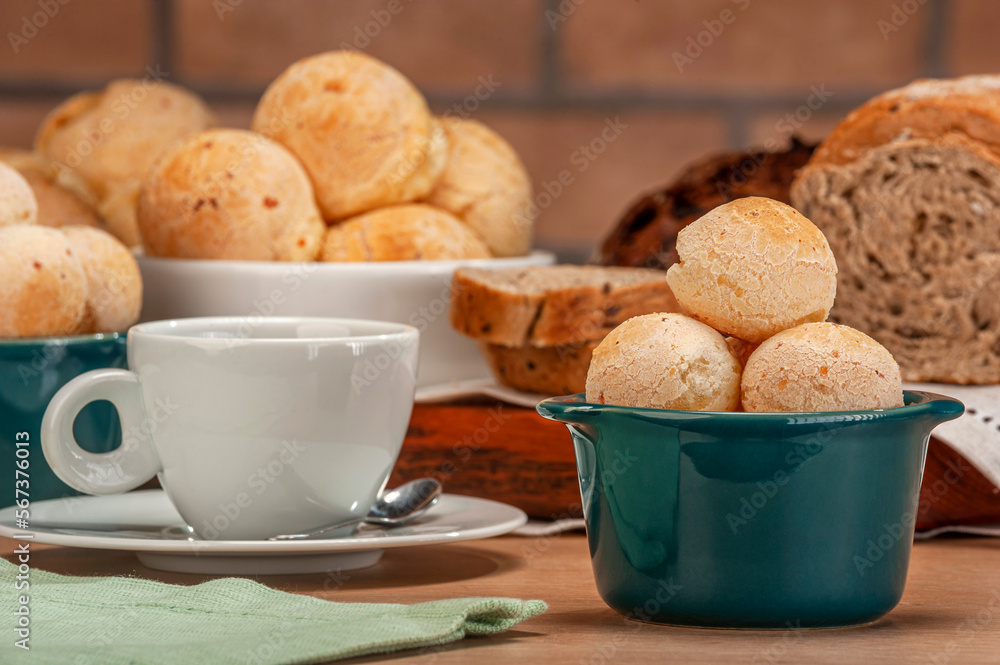Cheese breads in a green ramekin with a cup of coffee on wooden table and bricks wall background. Cheese breads in a green ramekin with a cup of coffee on wooden table and bricks wall background.