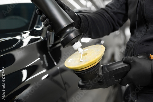 Professional detailing of the car in the auto studio, the master applies paste or wax to the car body polishing machine.