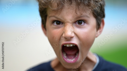 One angry young boy screaming to camera. Preteen child open mouth yelling in anger. Furious enraged male kid screaming