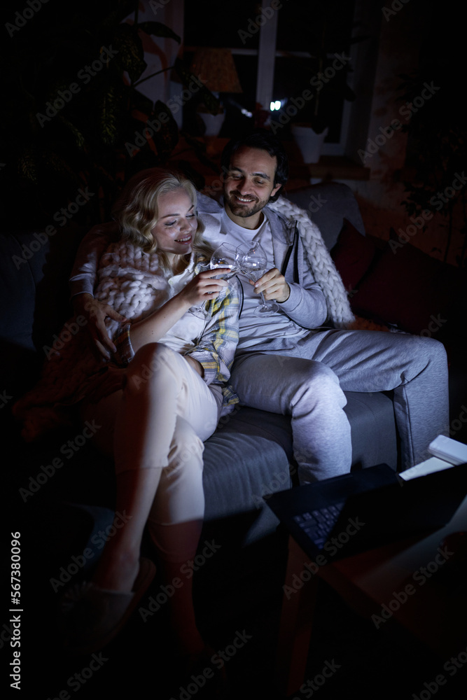 Cheers. Romantic date night. Young man and woman sitting together on couch at home in the evening and drinking wine. No electricity, blackout. Concept of power outage, relationship Cheers. Romantic date night. Young man and woman sitting together on couch at home in the evening and drinking wine. No electricity, blackout. Concept of power outage, relationship