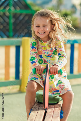 sunny summer day excited happy smiling face child girl in yellow dress play on colored wooden children playground in kindergarten vertical