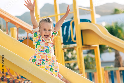 Child playing on outdoor wooden playground. Kids play on school or kindergarten yard. Active kid on colorful slide. Healthy summer activity for children