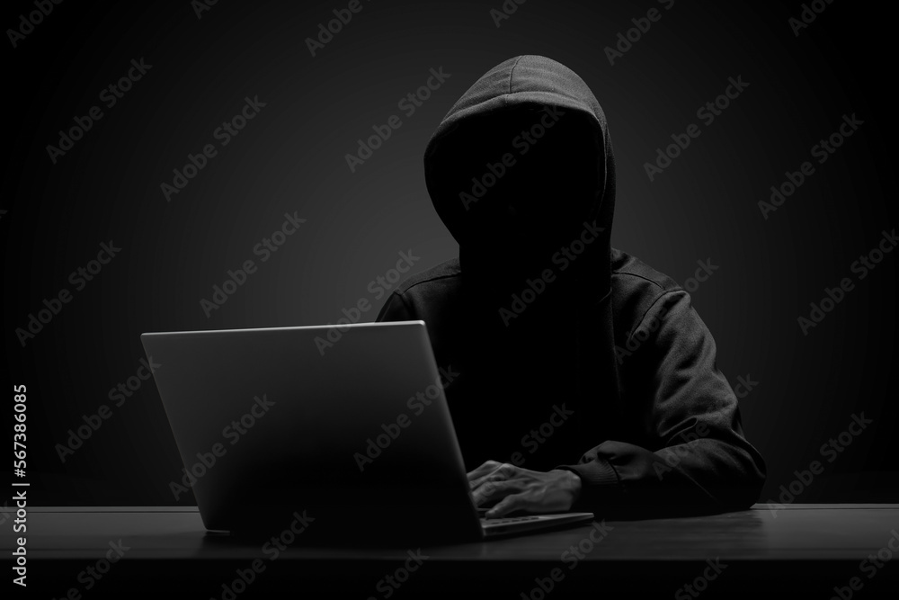 Mysterious man wearing black hoodie using laptop in the dark room. Hacker and cyber security concept. Mysterious man wearing black hoodie using laptop in the dark room. Hacker and cyber security concept.