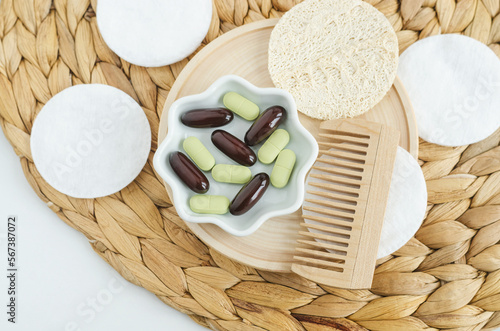 Small wooden plate with food supplement capsules, pills and wooden hairbrush. Natural healthcare, hair care and beauty treatment. Top view, copy space.