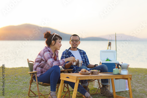 Asian couple having a cup of coffee or water at their camping site with lake in the background during sunset © ake1150