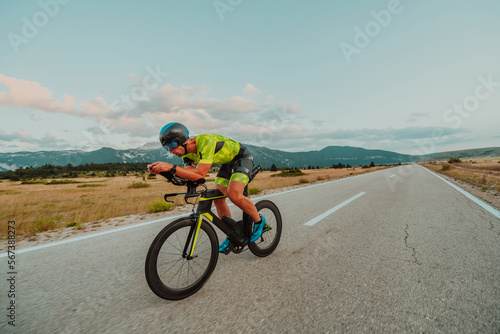 Fototapeta Naklejka Na Ścianę i Meble -  Full length portrait of an active triathlete in sportswear and with a protective helmet riding a bicycle. Selective focus 