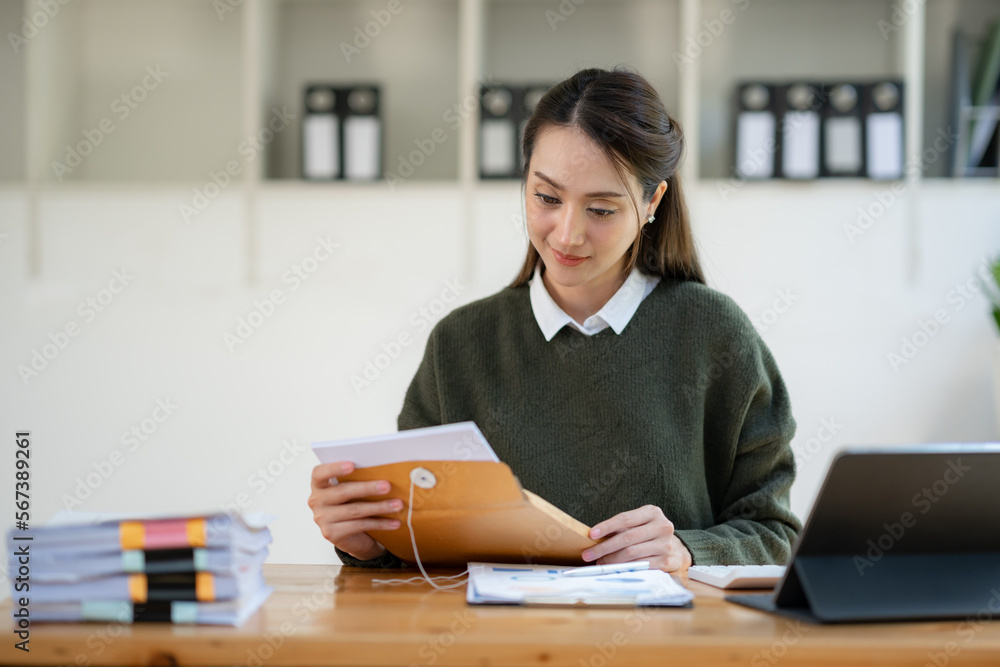 Asian businesswoman opening the brown envelope for details Information on accepting a business cooperation agreement. Asian businesswoman opening the brown envelope for details Information on accepting a business cooperation agreement.
