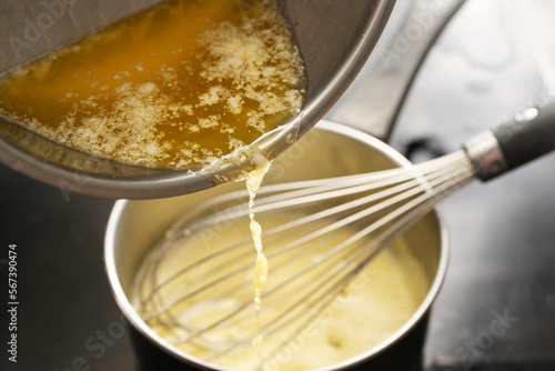 Cooking process of hollandaise sauce, pouring melted butter into the pot with egg mixture, whisking all the time at low temperature to get a creamy texture, selected focus