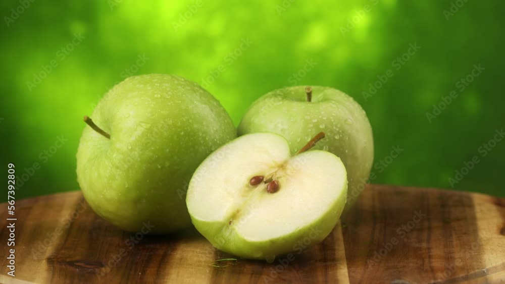 green apples with half cut are turned on a wooden board on a green background. fresh fruits with water drops close-up. High quality 4k footage green apples with half cut are turned on a wooden board on a green background. fresh fruits with water drops close-up. High quality 4k footage