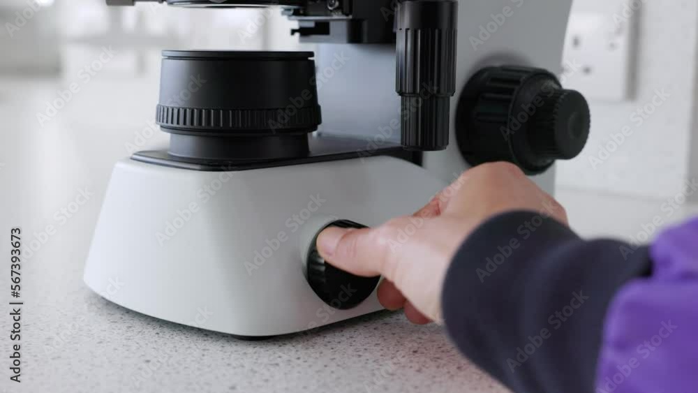scientist turning on microscope and adjusting microscope light source