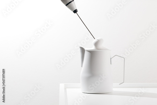 Making foamy milk with milk frother on a white table. photo